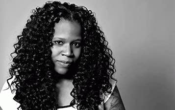 A Black woman with chest length curly hair. Author Naima Simone.